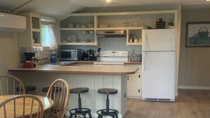 Une cuisine avec des meubles de rangement en bois, un réfrigérateur blanc, une cuisinière et un coin repas avec des chaises et des tabourets en bois.