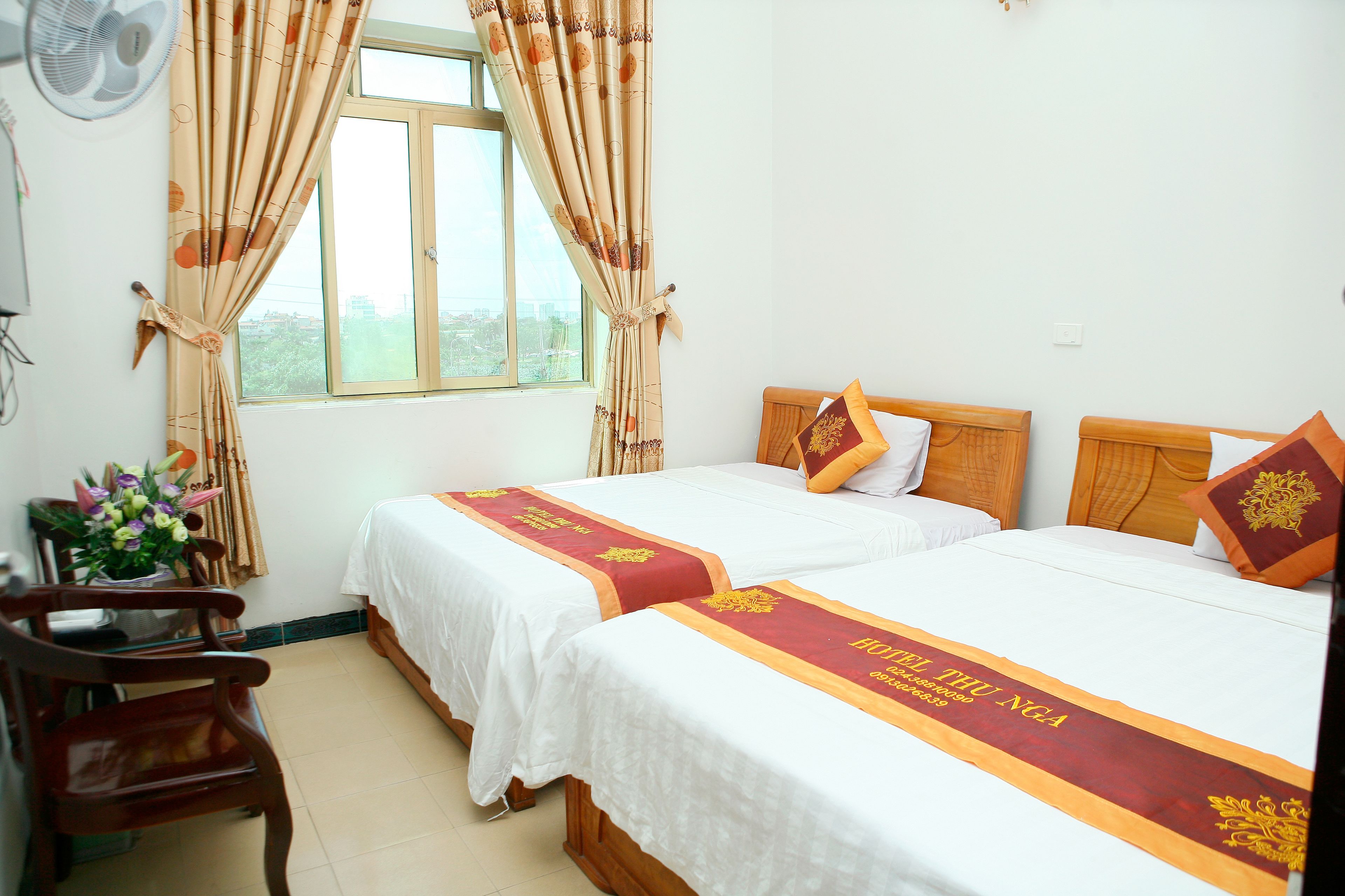 A hotel room with two beds, wooden headboards, white bedding, and a window with curtains.