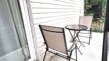 A covered patio with a metal table and two chairs, a sliding glass door, and a view of a backyard with a grill.