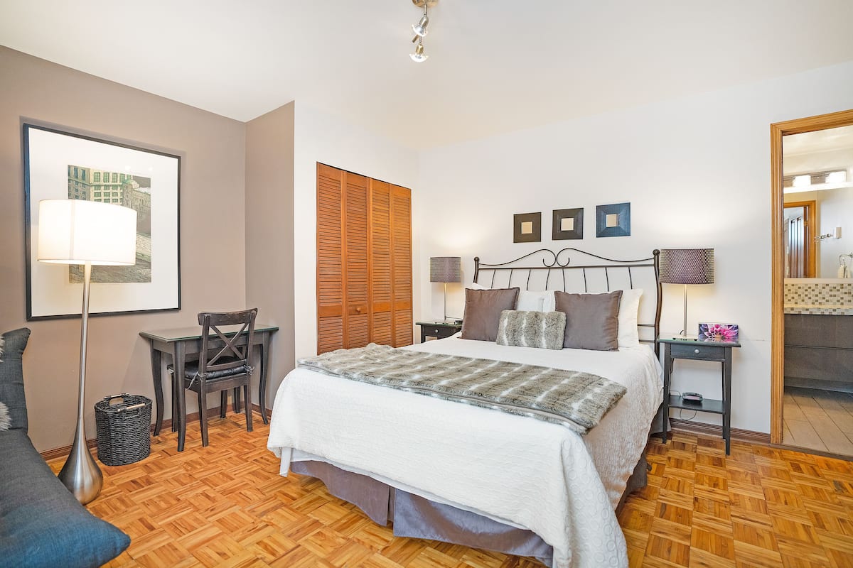 A neatly arranged bedroom with a bed, bedside tables, a chair, a lamp, and a wall-mounted picture.