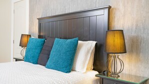 A neatly made bed with patterned bedding, a dark wooden headboard, and two bedside lamps on a glass table. - Accueil CHEZ Francois (Montreal)
