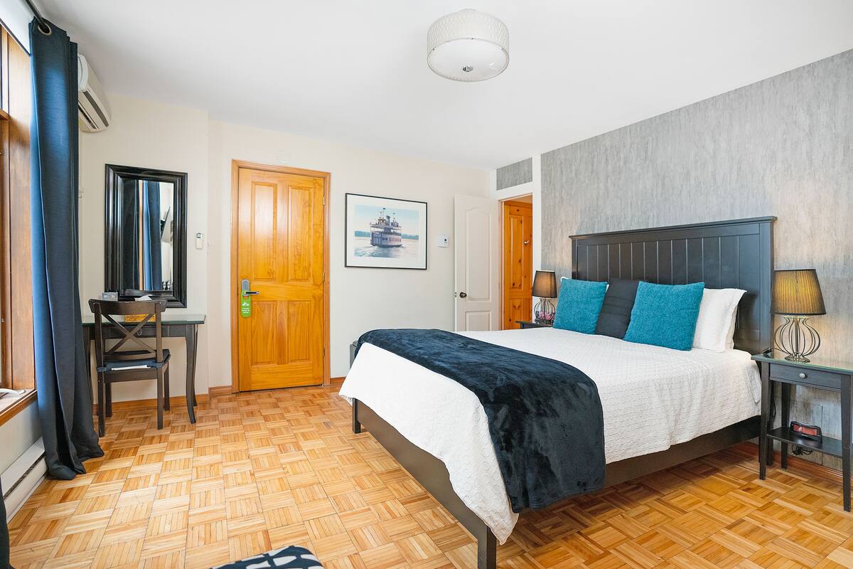 A hotel room with a bed, a desk, a chair, a lamp, and a picture on the wall.