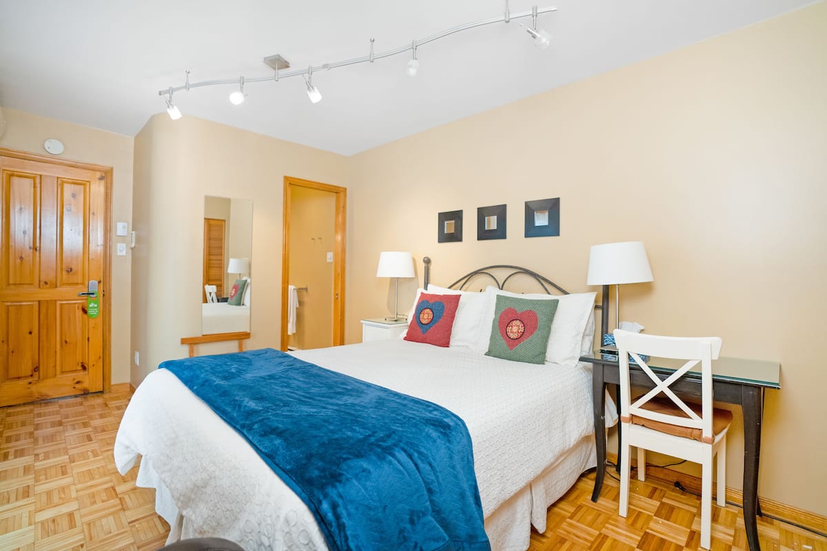 A bedroom with a bed, bedside table, lamp, chair, and a wooden door.