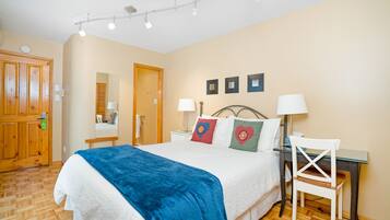 Un dormitorio con cama, mesita de noche, lámpara, silla y una puerta de madera.