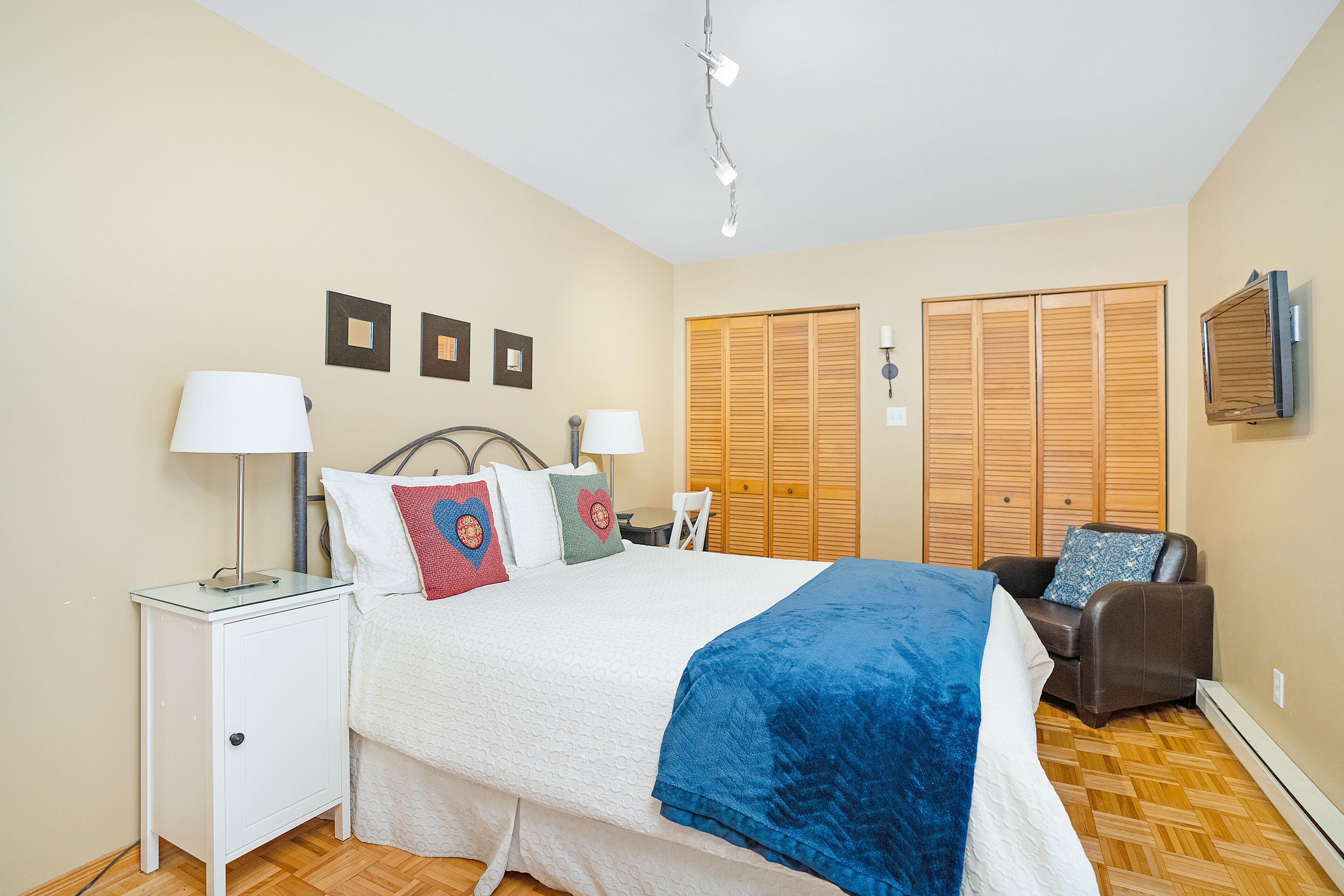 Une chambre à coucher comprenant un lit, des tables de chevet, une chaise, une armoire et un téléviseur.