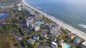 Oversigtsbillede af et kystresort med ejendomme ved stranden, en central pool og en lysthavn.