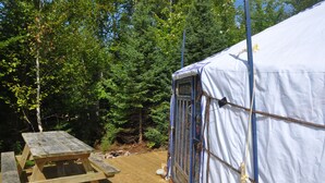 A wooden picnic table and a white tent in a forested area.