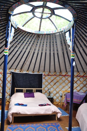 Experience the charm of a traditional yurt with a cozy bed, bedside table, and woven mat.