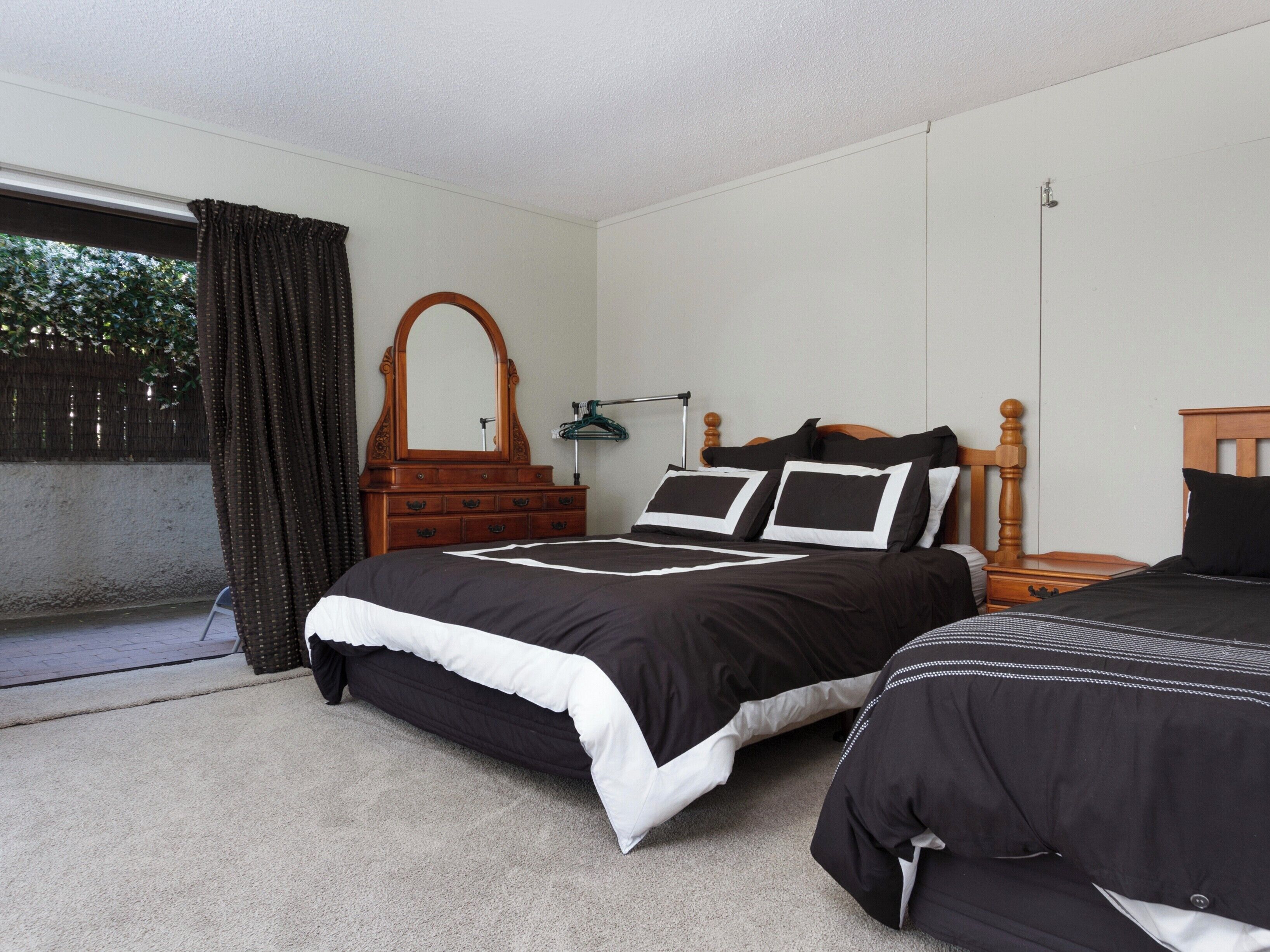 A bedroom with two beds, a wooden dresser, a mirror, and a window with curtains.