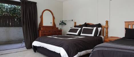 A bedroom with two beds, a wooden dresser, a mirror, and a window with curtains.