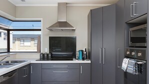 Una cocina moderna con gabinetes grises, una campana extractora de acero inoxidable, un horno empotrado y un ventanal con vista a una zona residencial.