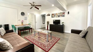 A modern living room with a sofa, a coffee table, a TV, and a dining area with chairs and a table. - Cozy Apartment unit is Available to Rent (Long Beach)
