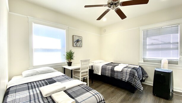 A hotel room with two beds, a desk, a ceiling fan, and a window with blinds. - Cozy Apartment unit is Available to Rent (Long Beach)