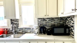 A kitchen with white cabinets, a coffee maker, a microwave, and a window with a view. - Cozy Apartment unit is Available to Rent (Long Beach)
