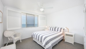 A bedroom with a bed, a chair, a nightstand, a ceiling fan, and a window with a view of the sea. - Craigmore On the Beach Unit 13 - One of the most desirable holiday locations in Yamba. (Yamba)