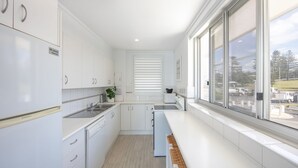 A modern kitchen with white cabinetry, a dishwasher, a sink, and a window overlooking a residential area. - Craigmore On the Beach Unit 13 - One of the most desirable holiday locations in Yamba. (Yamba)