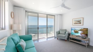 A living room with a teal sofa, a television, and a balcony with a view of the sea. - Craigmore On the Beach Unit 13 - One of the most desirable holiday locations in Yamba. (Yamba)