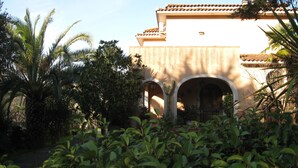 A building with a tiled roof and arched doorways, surrounded by lush greenery and a palm tree.