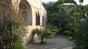 A building with arched windows and a pathway leading to it, surrounded by greenery.