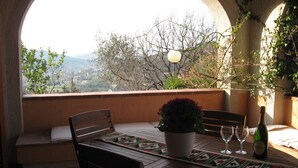 An outdoor dining area with a table, chairs, a bottle of wine, and a view of the countryside.