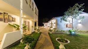 A well-lit pathway leading to a building with a modern design, surrounded by greenery and potted plants. - The Story Resort Bohol (Panglao)