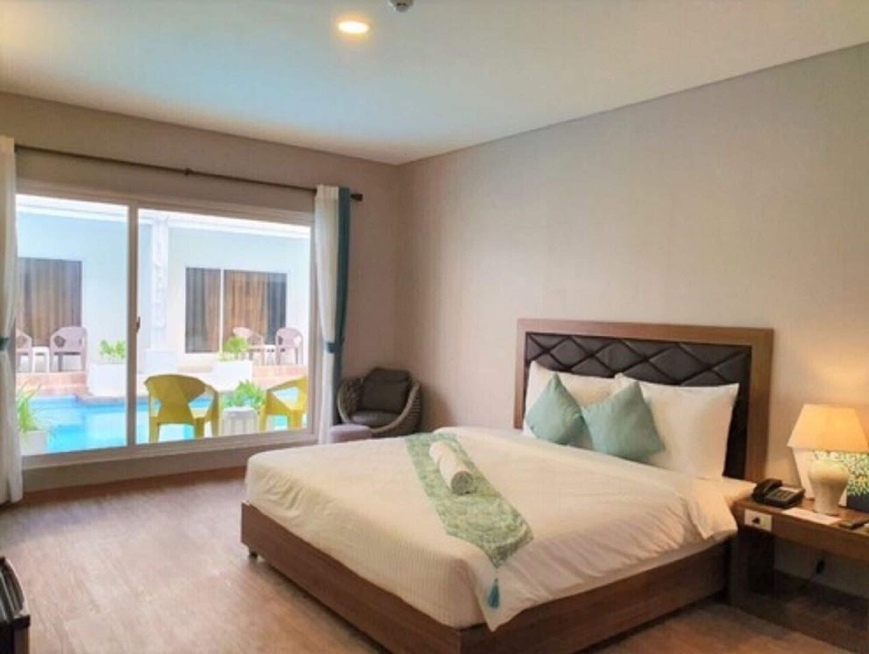 A hotel room with a bed, a nightstand, a chair, a view of a pool, and a balcony.