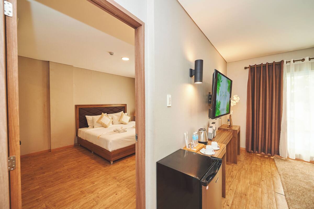 A hotel room with a bed, a desk with a television, and a window with curtains.