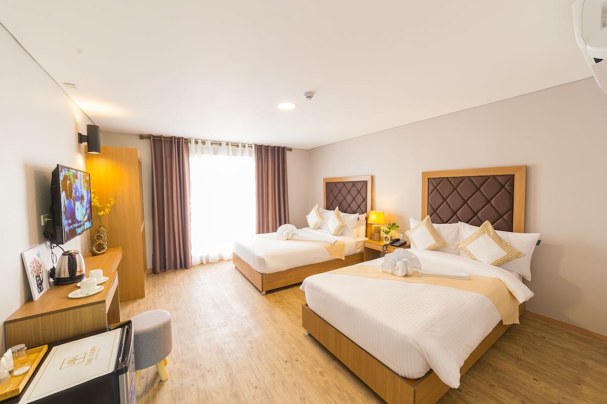 A hotel room with two beds, a desk with a computer and a coffee maker, a TV, and a window with curtains.