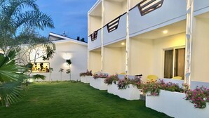 A two-story building with a flat roof, white exterior walls, and a small garden area with grass and flowering plants. - The Story Resort Bohol (Panglao)