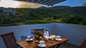 A wooden table with a bowl of fruit, milk, and cups on a balcony overlooking a hillside. - Enjoy your private pool and outdoor kitchen (Marina)