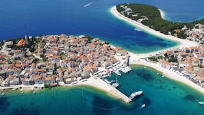 An aerial view of a coastal town with a central island featuring dense buildings, a marina, and a beach. - Enjoy your private pool and outdoor kitchen (Marina)