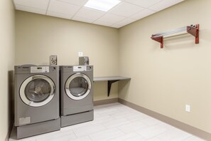A laundry room with two front-loading washing machines, a shelf, and a wall-mounted heater. - Holiday Inn Express & Suites Springfield North (Springfield)