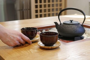 Una mesa de madera con dos tazas de cerámica oscura sobre platillos y una tetera negra con asa.