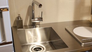 A stainless steel kitchen sink with a modern faucet, a built-in soap dispenser, and a compact countertop. - Kotobuki Sou (Tokyo)