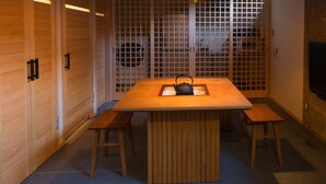 A room with a wooden table, two benches, a TV mounted on the wall, and a traditional Japanese screen in the background. - Kotobuki Sou (Tokyo)