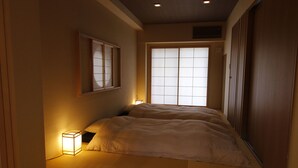 A traditional Japanese-style bedroom with tatami flooring, a shoji screen window, and a bedside table with a lamp. - Kotobuki Sou (Tokyo)