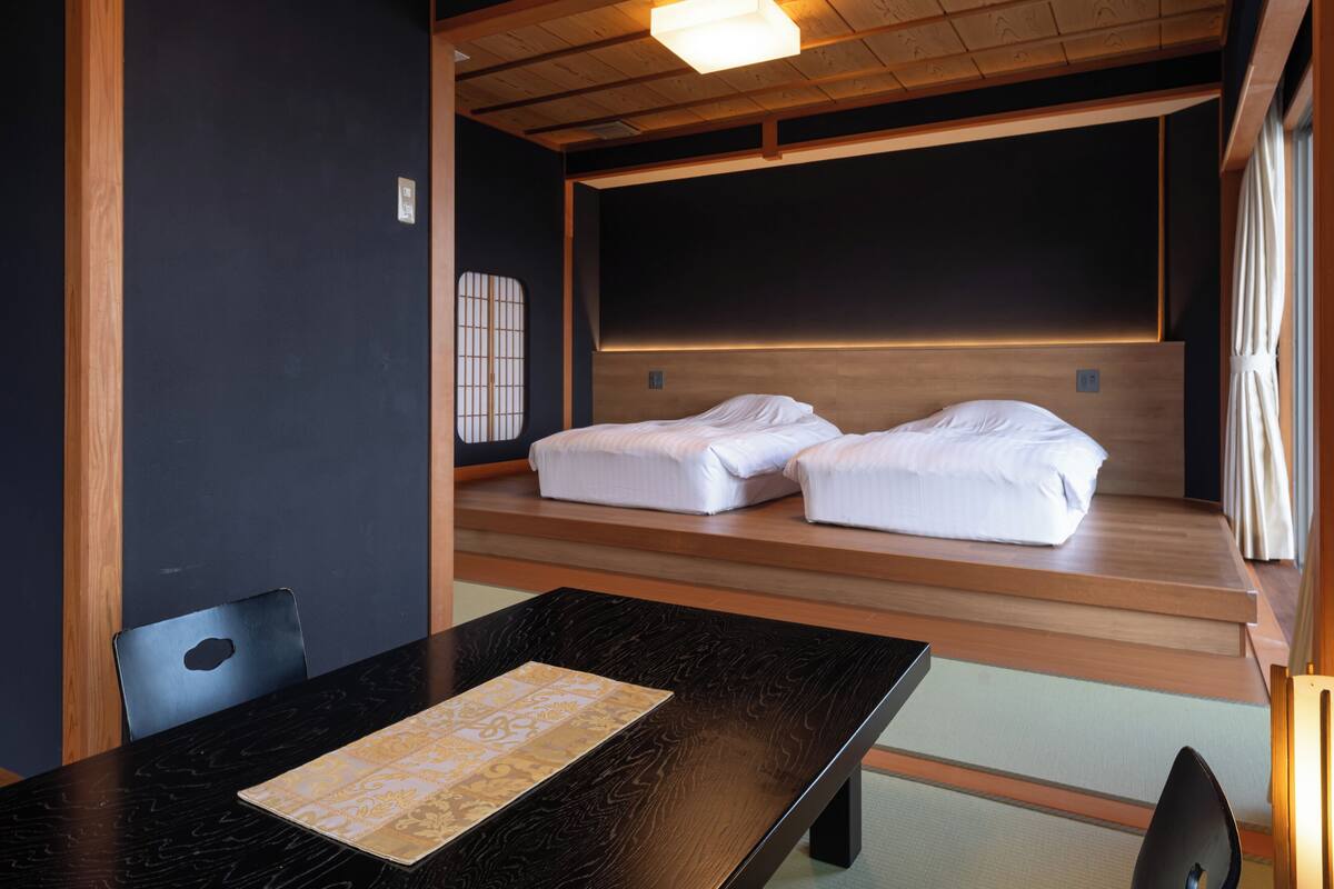 A traditional Japanese room with tatami flooring, a low wooden ceiling, and a futon bed.