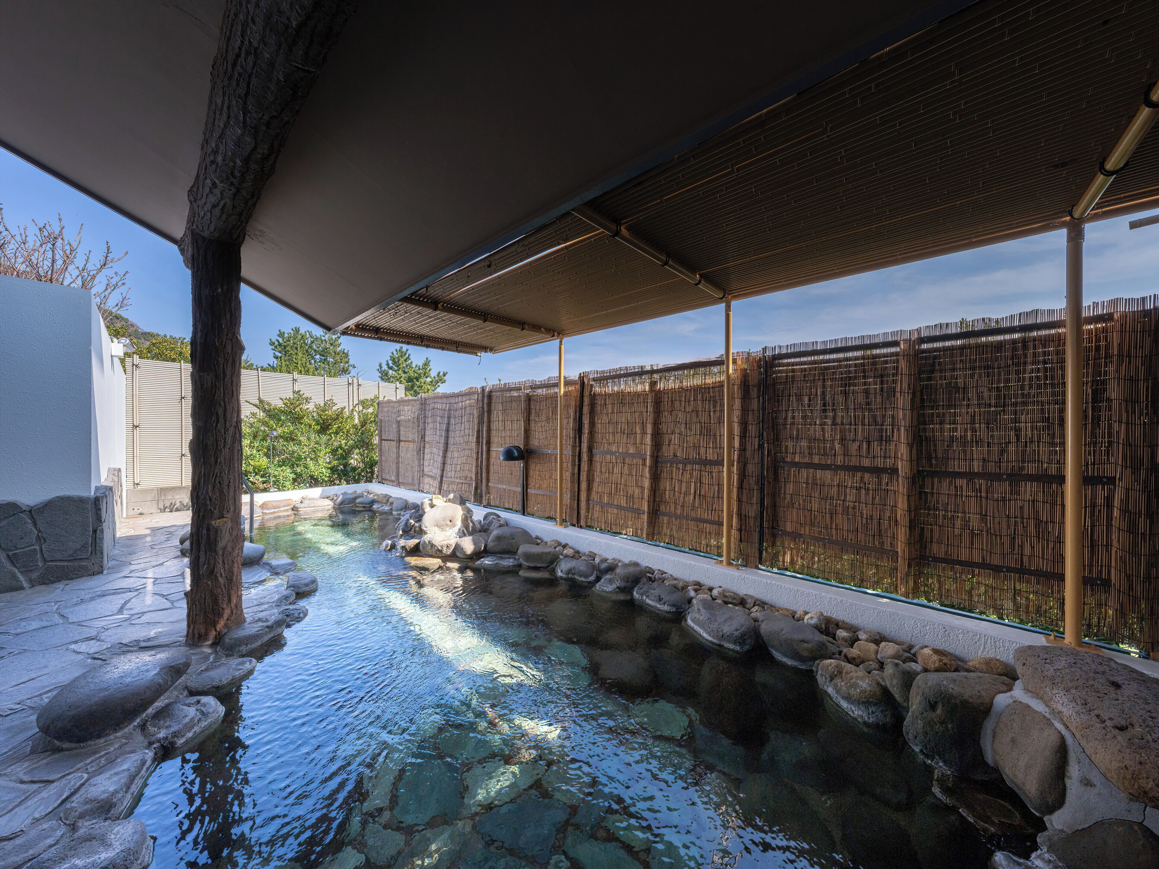 Una piscina bordeada de piedra, con valla de bambú y pérgola.