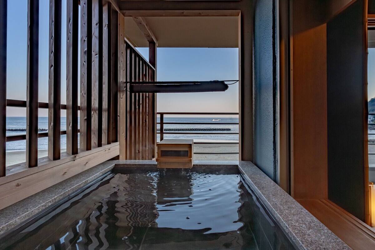 A wooden interior with a view of the ocean, a small wooden bench, and a water feature.