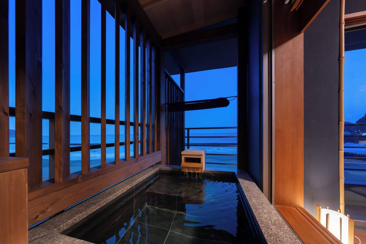 A spa area with a wooden deck overlooking the ocean, a small wooden bench, and a hot tub.