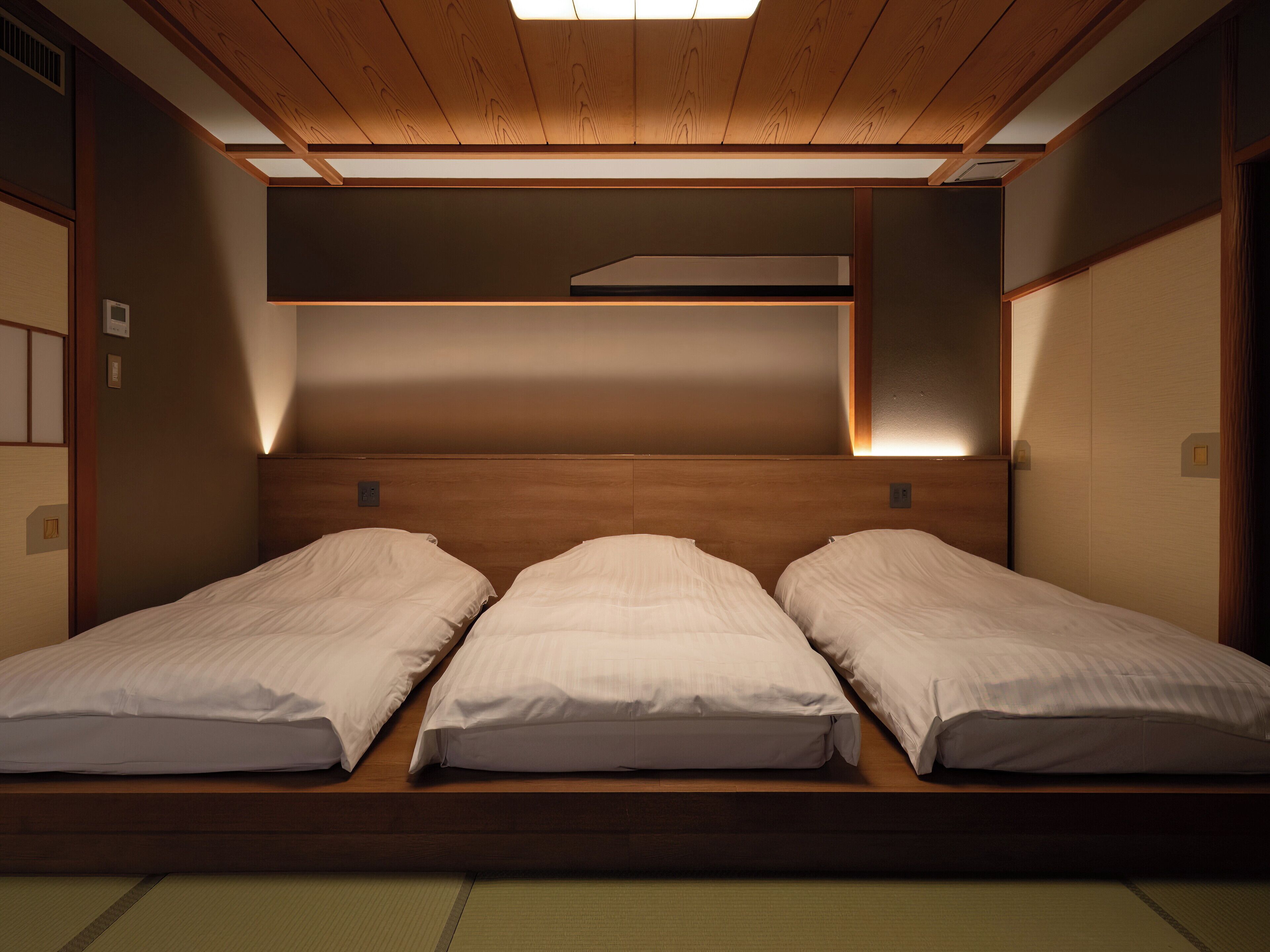 Una habitación con tres camas individuales alineadas, cabeceros de madera y un techo inclinado con tragaluz.