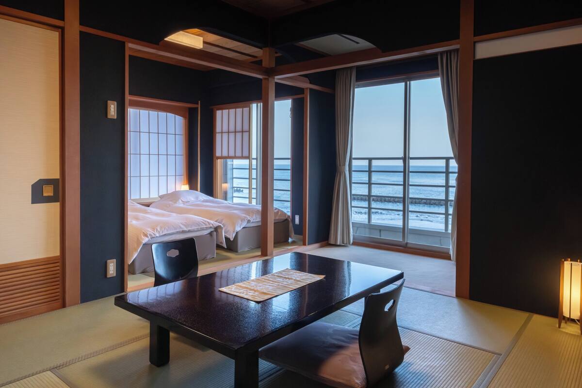 A traditional Japanese-style room with tatami flooring, a low table, and a bed with a view of the sea.