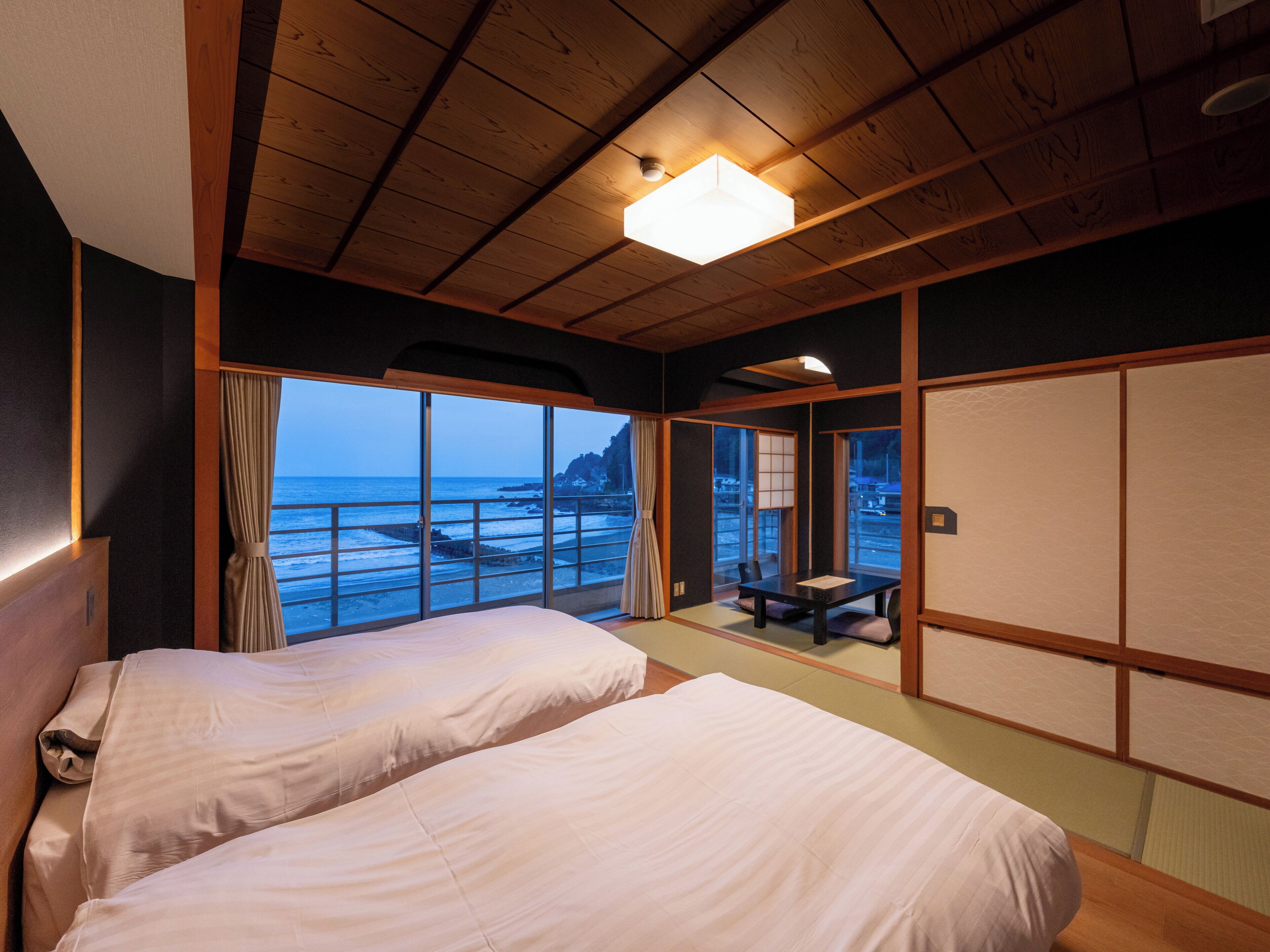 A traditional Japanese-style room with tatami flooring, a low ceiling, and a large window overlooking the sea.