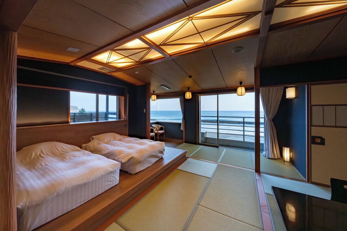 A room with two beds, tatami mats, a view of the sea, and a sliding door.