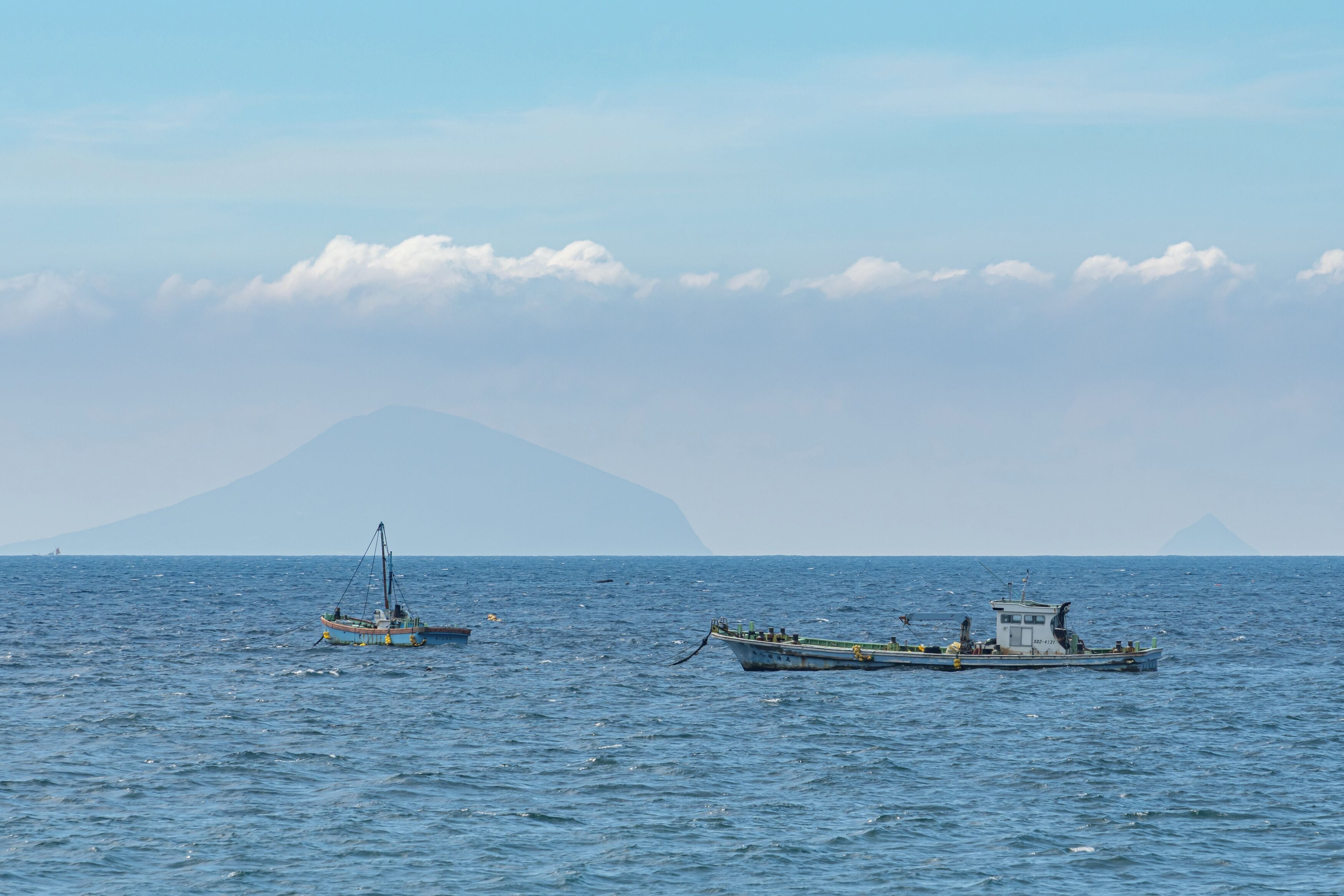 Dos barcos sobre aguas marinas tranquilas, con una montaña al fondo.