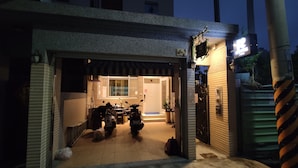 L’entrée d’un garage où est garée une moto, avec une plante en pot et un vélo à proximité.