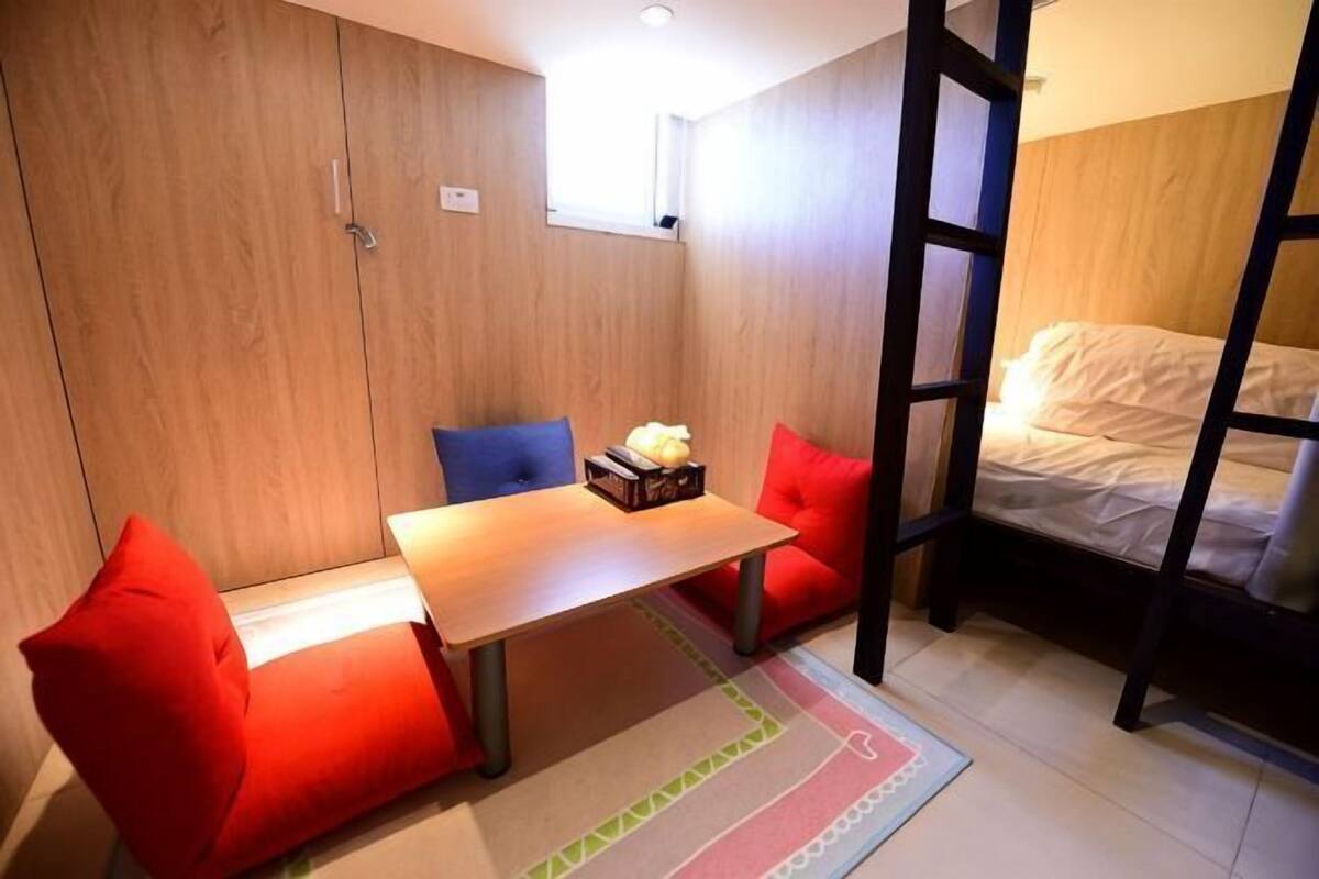 A compact room with a bed, a small table, and two red chairs.