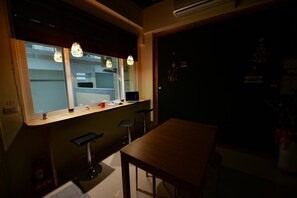 A kitchen with a window, bar stools, a wooden table, and a refrigerator. - K2 Hostel (Taitung)