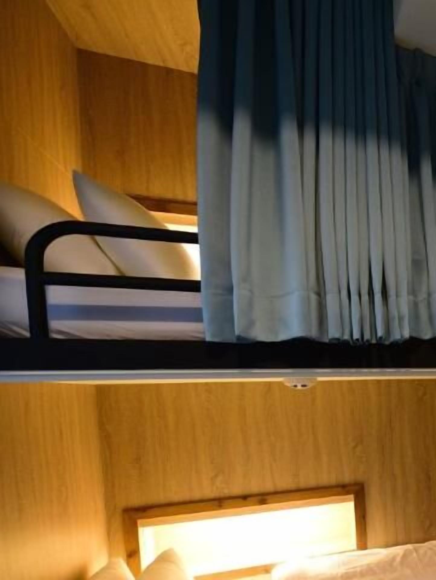A bunk bed with a headboard, a window with curtains, and a bedside table with a lamp.