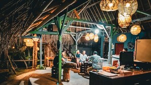 An outdoor dining area with a thatched roof, wooden tables, and hanging lanterns. - Gading Treehouse (Penida Island)